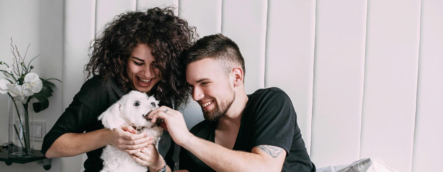 a man and woman sitting on a bed playing with a dog